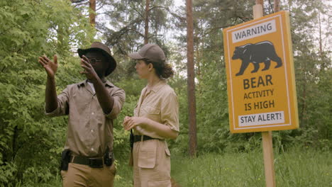 Schild,-Um-Vor-Hoher-Bärenaktivität-Im-Wald-Und-Zwei-Rangern-Zu-Warnen,-Die-Sich-In-Der-Nähe-Unterhalten