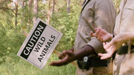 Nahaufnahme-Von-Afroamerikanischen-Försterhänden,-Die-Ein-Schild-Halten,-Um-Zu-Warnen,-Dass-Es-Wilde-Tiere-Im-Wald-Gibt