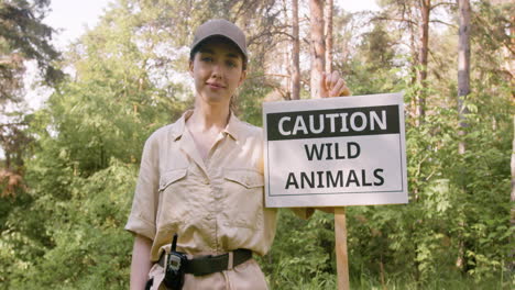 Caucasian-female-forest-warden-holding-a-signboard-to-warn-that-there-are-wild-animals-in-the-woods