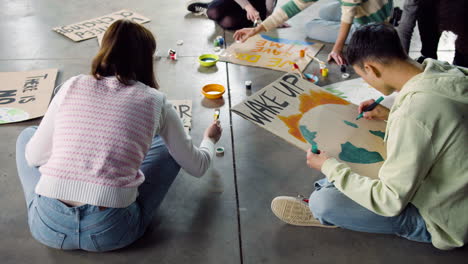 Young-environmental-activists-painting-placards-sitting-on-the-floor