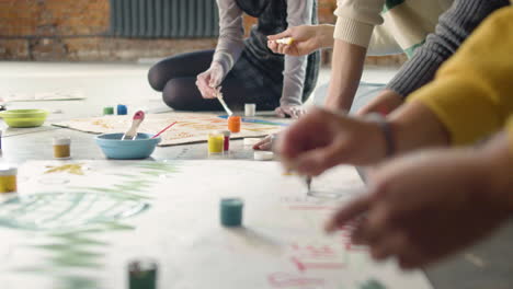 Close-up-of-unrecognizable-environmental-activists-painting-placards-sitting-on-the-floor