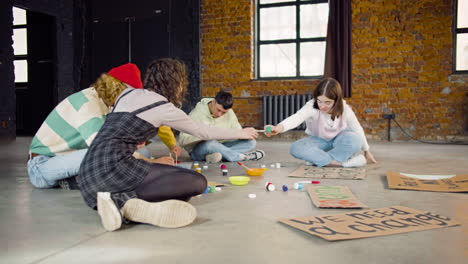 Young-environmental-activists-painting-placards-sitting-on-the-floor