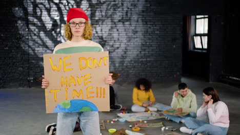 Serious-young-environmental-activist-holding-a-cardboard-with-We-don't-have-time"-inscription-and-looking-at-the-camera"