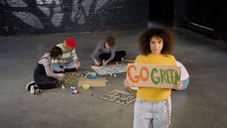 Young-environmental-activist-holding-a-cardboard-with-Go-green"-inscription-and-looking-at-the-camera"