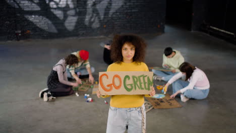 Young-environmental-activist-holding-a-cardboard-with-Go-green"-inscription-and-looking-at-the-camera"