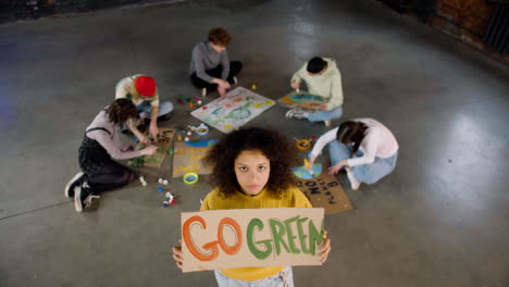 Top-view-of-a-young-environmental-activist-holding-a-cardboard-with-Go-green"-inscription-and-looking-at-the-camera"