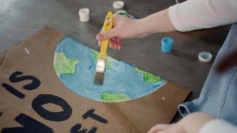 Close-up-of-unrecognizable-environmental-activist-painting-placards-sitting-on-the-floor