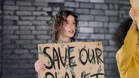 Young-environmental-activist-holding-a-cardboard-with-Save-our-planet"-inscription-and-protesting-with-her-friend-against-climate-change-inaction"