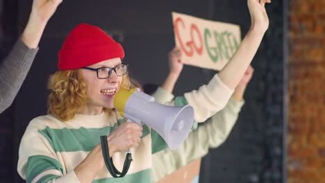 Young-environmental-activist-holding-megaphone-and-protesting-with-her-friends-against-climate-change-inaction