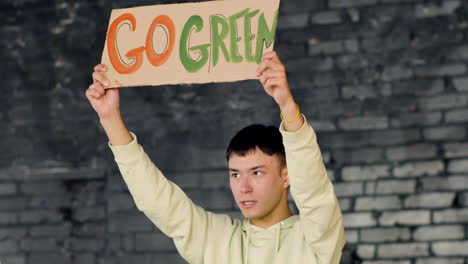 Young-Asian-environmental-activist-holding-a-cardboard-with-Go-green"-inscription-and-protesting-against-climate-change-inaction"