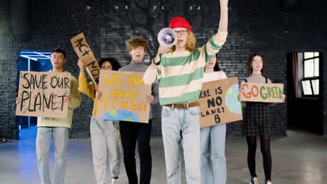 Vorderansicht-Junger-Umweltaktivisten-Mit-Plakaten-Und-Megaphon,-Die-Auf-Die-Kamera-Zugehen-Und-Gegen-Die-Untätigkeit-Des-Klimawandels-Protestieren