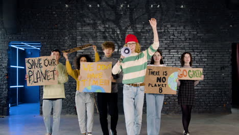 Front-view-of-young-environmental-activists-with-placards-and-megaphone-walking-towards-camera-and-protesting-against-climate-change-inaction