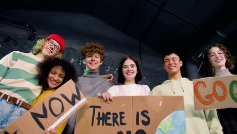 View-from-below-of-happy-young-environmental-activists-holding-cardboard-placards-and-looking-at-the-camera