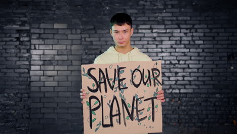 Joven-Activista-Ambiental-Asiático-Sosteniendo-Un-Cartón-Con-La-Inscripción-&quot;salvar-El-Planeta&quot;-Y-Mirando-La-Cámara