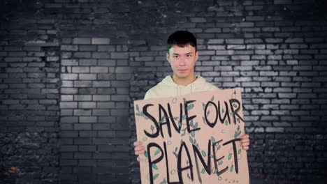 Joven-Activista-Ambiental-Asiático-Sosteniendo-Un-Cartón-Con-La-Inscripción-&quot;salvar-El-Planeta&quot;-Y-Protestando-Mientras-Mira-La-Cámara&quot;