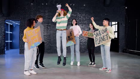 Happy-young-environmental-activists-with-placards-and-megaphone-jumping-and-protesting-against-climate-change-inaction