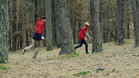 Caucasian-cheerful-father-and-son-in-red-capes-running-in-the-forest-and-playing-they-being-superheroes