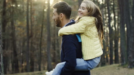 Handsome-Caucasian-man-spinning-his-pretty-little-daughter-on-his-back-while-she-closing-his-eyes-in-the-forest