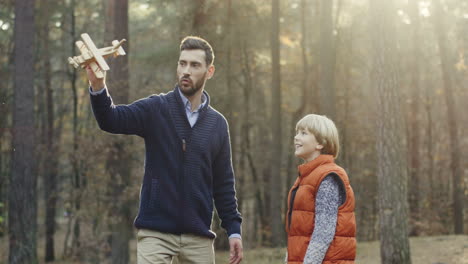 Caucasian-handsome-man-playing-with-his-little-cute-son-with-a-wooden-plane-in-the-forest