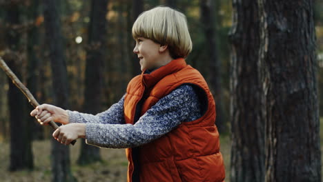 Cute-Caucasian-blond-boy-playing-with-a-stick-in-the-forest-cheerfully