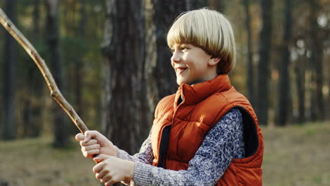 Close-up-view-of-cute-Caucasian-blond-boy-playing-with-a-stick-in-the-forest-cheerfully