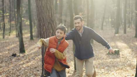 Cute-small-Caucasian-boy-running-in-the-wood-and-his-father-following-his-as-trying-to-catch-him-while-they-playing
