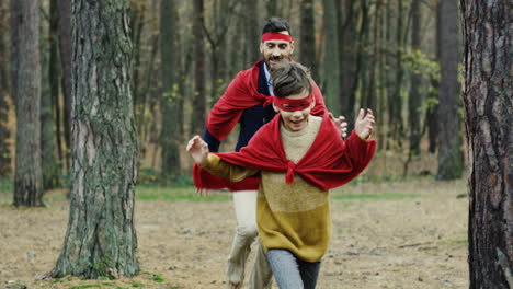 Happy-Caucasian-dad-and-his-small-son-playing-being-superheroes-with-red-capes-in-the-forest