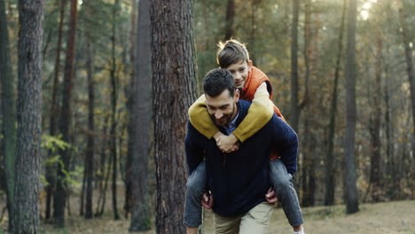 Handsome-Caucasian-man-giving-her-little-son-a-piggyback-in-the-forest