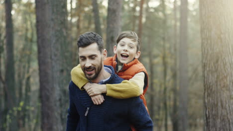 Close-up-view-of-handsome-Caucasian-man-giving-her-little-son-a-piggyback-in-the-forest