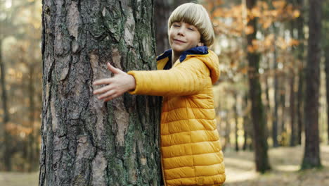 Side-view-of-a-cute-little-teen-boy-hugging-a-tree-trunk-with-eyes-closed-in-the-forest