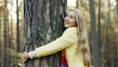 Close-up-view-of-a-cute-teen-girl-hugging-a-tree-trunk-with-eyes-closed-in-the-forest