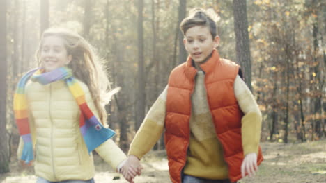 Cheerful-Caucasian-girl-and-boy-running-in-the-forest-and-holding-hands-on-a-sunny-day