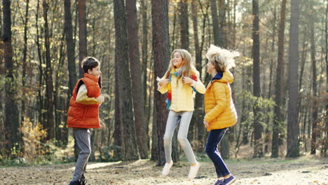 Close-up-view-of-joyful-kids,-girl-and-two-boys,-laughing,-jumping-and-having-fun-in-the-forest-on-a-sunny-day