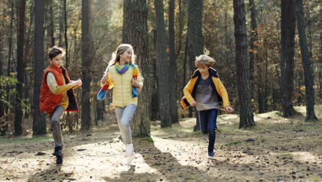 Joyful-kids,-girl-and-two-boys,-running-and-having-fun-in-the-forest-on-a-sunny-day