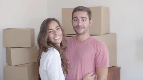 Caucasian-couple-standing-in-new-house-while-hugging-and-looking-at-the-camera