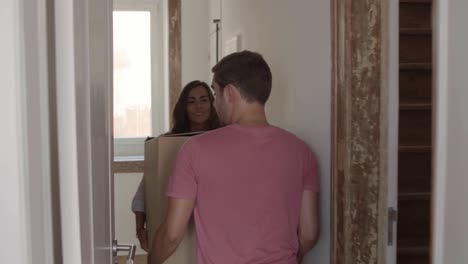Young-couple-moving-to-new-house,-carrying-big-box-together-and-putting-it-in-living-room