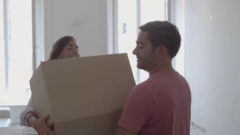Happy-man-coming-into-room,-carrying-box-with-different-stuff,-kissing-and-hugging-young-wife
