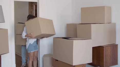 Young-boyfriend-and-girlfriend-entering-room-and-carrying-cardboard-boxes