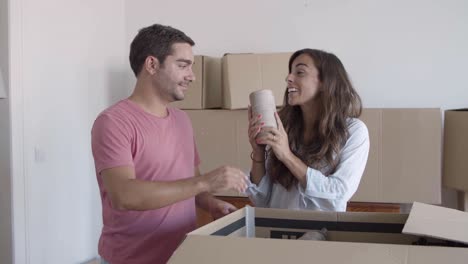 Happy-couple-unpacking-cardboard-boxes-with-stuff,-talking-and-smiling