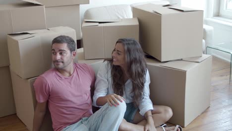 Young-Caucasian-couple-sitting-on-floor-near-carton-boxes-and-discussing-interior