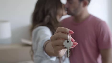 Unfocused-happy-woman-holding-keys-from-new-apartment,-showing-them-at-the-camera-and-kissing-boyfriend
