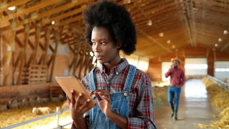 Young-African-American-woman-farmer-using-a-tablet-and-thinking-in-a-stable