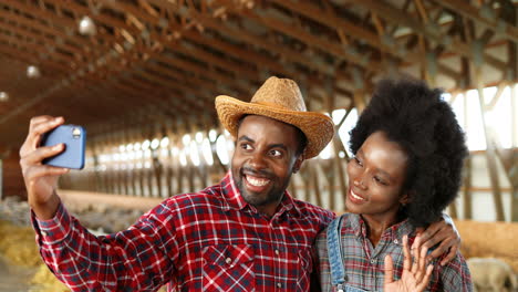 African-American-woman-and-man-farmers-with-denim-jumpsuit-making-a-selfie-with-smartphone-in-a-stable