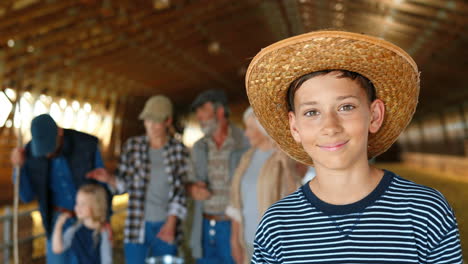 Portrait-of-Caucasian-teen-boy-in-hat-standing-in-stable-and-smiling-at-camera