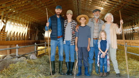 Portrait-of-happy-Caucasian-family-of-farmers-standing-in-a-stable-with-livestock-and-smiling-to-camera