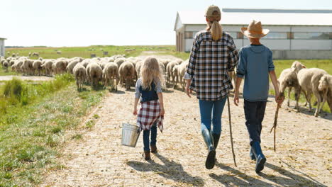 Rear-view-of-Caucasian-mother-farmer-walking-with-her-son-and-daughter-while-the-sheep-flock-is-grazing
