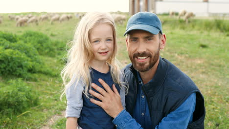 Portrait-of-Caucasian-young-father-with-cute-little-daughter-and-smiling-at-camera-in-green-field