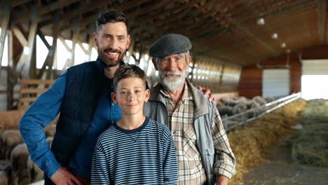 Grandfather,-father-and-grandson-farmers-looking-at-camera-in-a-stable-with-sheep-flock