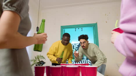 Happy-multiethnic-young-friends-playing-beer-pong-at-home