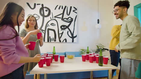 Multiethnic-young-friends-playing-beer-pong-at-home